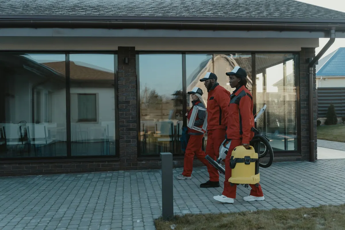 A cleaning crew in uniform carrying a vacuum and equipment up to a client's front door